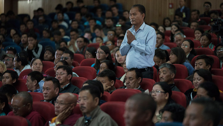Один из слушателей встает в то время, как ведущий зачитывает его вопрос Его Святейшеству Далай-ламе. Фото: Тензин Чойджор (офис ЕСДЛ)