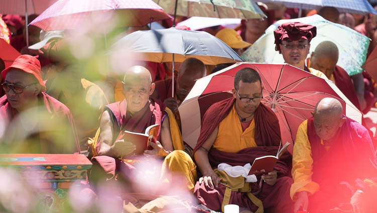 Прячась под зонтиками от палящих лучей солнца, монахи следят по тексту за Его Святейшеством Далай-ламой, читающим поэму Шантидевы «Путь бодхисаттвы». Фото: Тензин Чойджор (офис ЕСДЛ)