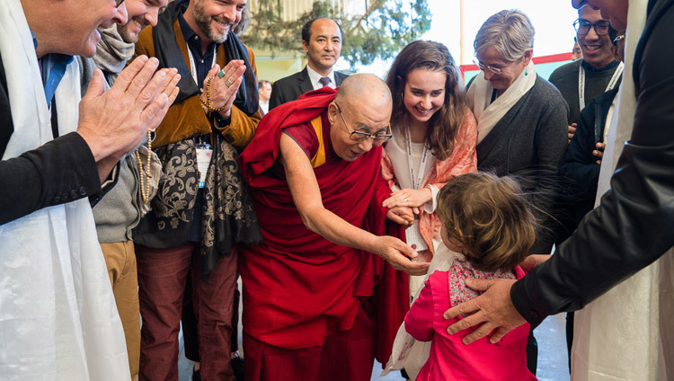 Его Святейшество Далай-лама тепло приветствует маленькую девочку, направляясь в главный тибетский храм в начале заключительного дня XXXIII конференции института «Ум и жизнь» на тему «Новый взгляд на процветание человечества». Фото: Тензин Чойджор.