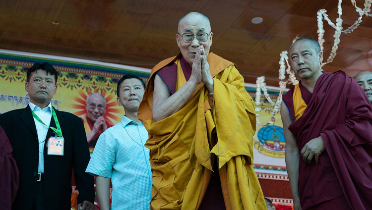 Его Святейшество Далай-лама приветствует верующих, поднявшись на сцену на площадке для проведения учений монастыря Самстанлинг. Фото: Тензин Чойджор.