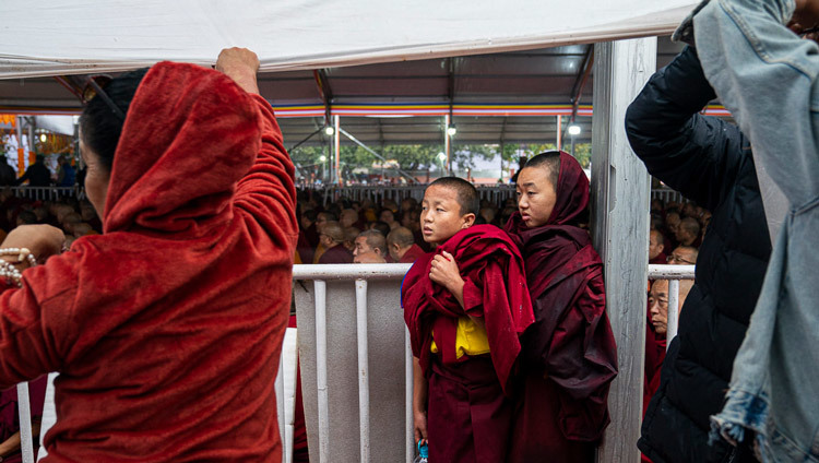 Юные монахи прячутся от дождя, в то время как Его Святейшество Далай-лама обращается к собравшимся перед посвящением Авалокитешвары. Фото: Тензин Чойджор.