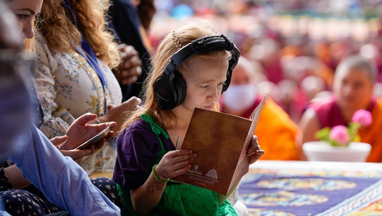 Маленькая девочка слушает синхронный перевод и следит за текстом во время учений Его Святейшества Далай-ламы по сочинению «Тридцать семь практик бодхисаттвы». Ле, Ладак, Индия. 21 июля 2023 г. Фото: дост. Замлинг Норбу (офис ЕСДЛ).